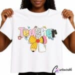 White T-shirt with a colourful “Teacher” DTF transfer design featuring patterned letters, daisies, an apple, school supplies, and a large yellow bow.