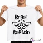 White T-shirt with a black “Braai Kaptein” DTF transfer design featuring bold Afrikaans text and a shield emblem with wings and a star.