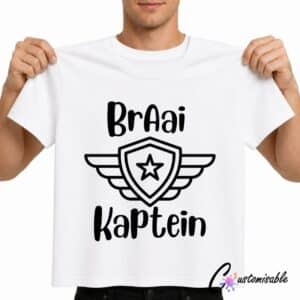 White T-shirt with a black “Braai Kaptein” DTF transfer design featuring bold Afrikaans text and a shield emblem with wings and a star.