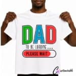 White T-shirt with colourful “Dad To Be Loading Please Wait” DTF transfer design featuring bold red, green, and blue letters with a loading bar graphic.