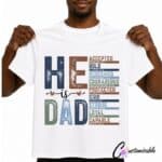 White T-shirt with faith-based “He Is Dad” DTF transfer design featuring Bible words including accepted, bold, redeemed, courageous, protected, kind, strong, loyal, and capable.