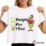 White T-shirt with Christmas DTF transfer design reading “Naughty Nice I Tried” with checkbox graphics and a green festive character wearing a Santa outfit.