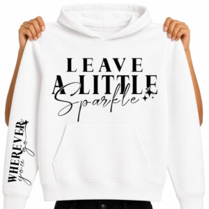 A mockup of a white pullover hoodie with a front pocket displaying a black DTF transfer design. The chest features the quote "LEAVE A LITTLE Sparkle" in a mix of elegant serif typography and cursive script, complete with small accent starburst sparkles. The right sleeve displays a vertical matching print that reads "WHEREVER you go" with small heart flourishes. The hoodie is held up by a model against a white background to clearly showcase the dual placement apparel print design.